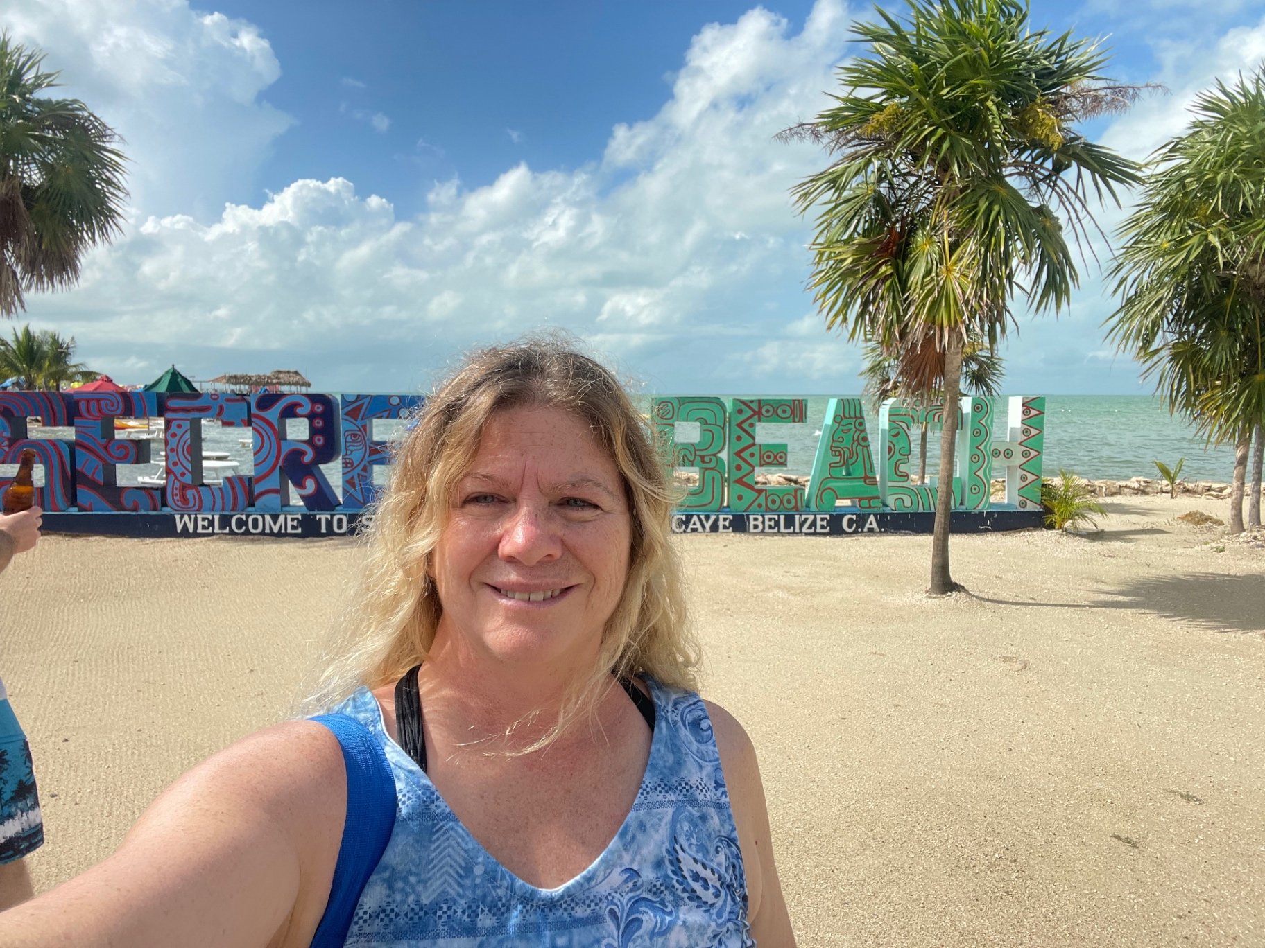 Misty Daugherty at the Secret Beach sign on Ambergris Caye, Belize, with palms and turquoise Caribbean water