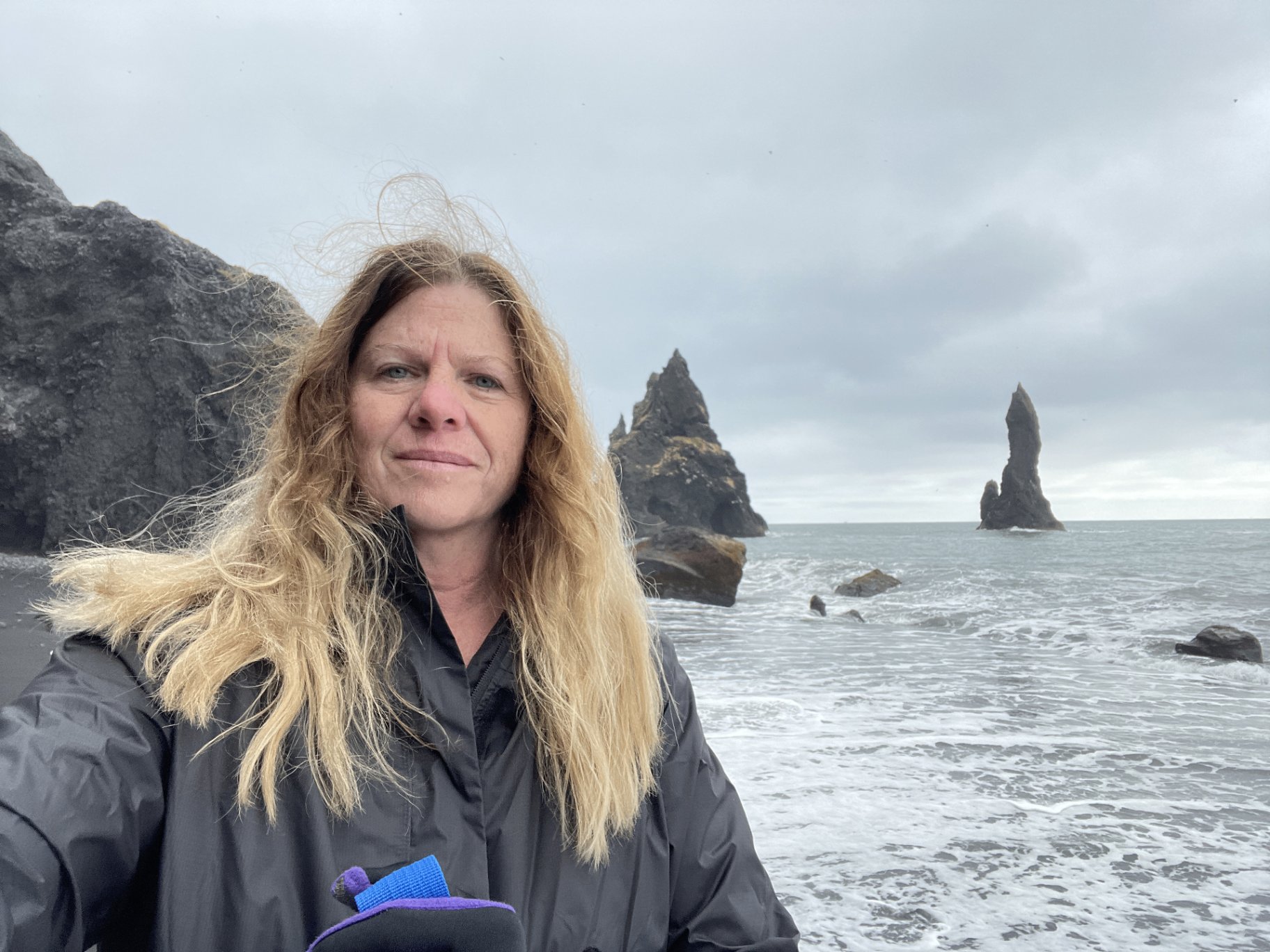 Misty Daugherty on Reynisfjara black sand beach in Iceland with the Reynisdrangar sea stacks behind her